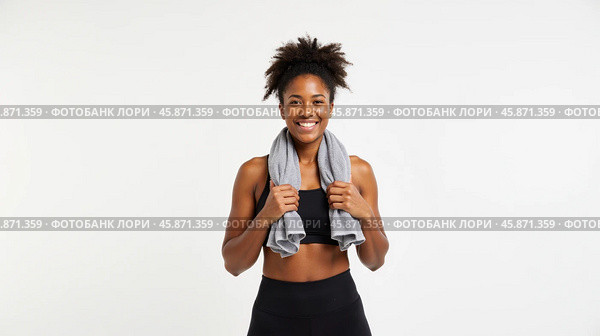 Fit woman smiling after workout holding towel around shoulders wearing sportswear looking energized healthy happy isolated on white background. Стоковое AI-изображение, AI-художник Павел Муравьев / Фотобанк Лори