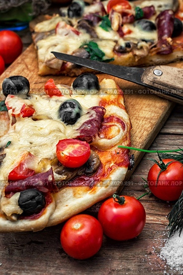 flavorful homemade pizza with bacon. hunk of delicious meat pizza with bacon and olives on the background of the vegetables.The image is tinted. Стоковое фото, агентство Ingram Publishing / Фотобанк Лори
