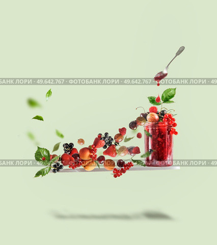 Flying cutting board with red jam jar, spoon and various berries:  currants, strawberries, raspberries, cherries, gooseberries and apricots at pale green background. Creative food levitation. Стоковое фото, агентство Ingram Publishing / Фотобанк Лори