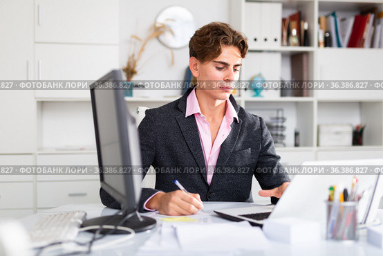 Focused attractive young man working with laptop and documents. Стоковое фото, фотограф Яков Филимонов / Фотобанк Лори
