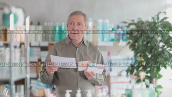 Focused elderly man in casual clothes comparing medications to doctor prescription note at pharmacy, carefully choosing right medications. Стоковое видео, видеограф Яков Филимонов / Фотобанк Лори