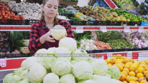 Focused girl working as a saleswoman in a store lays out cabbages on the counter. Стоковое видео, видеограф Яков Филимонов / Фотобанк Лори