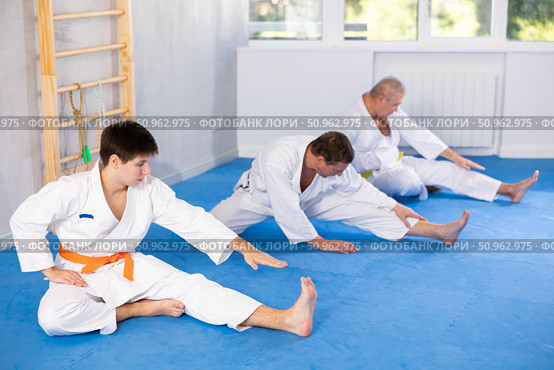 Focused guy in kimono stretching after group martial arts training. Стоковое фото, фотограф Яков Филимонов / Фотобанк Лори