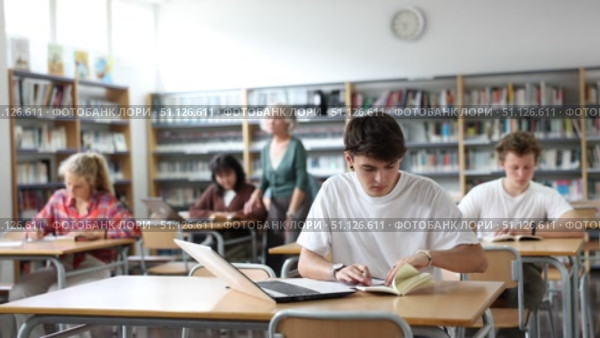 Focused teenager male student sitting at library desk, preparing for exam. Стоковое видео, видеограф Яков Филимонов / Фотобанк Лори
