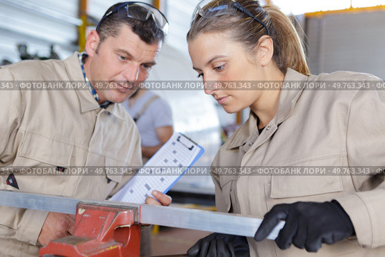foreman watching female worker clamp metal into vice. Стоковое фото, агентство Ingram Publishing / Фотобанк Лори