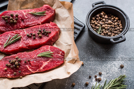 Fresh meat. Raw beef steaks with rosemary and spices on parchment paper on a stylish board. Flat top view. Стоковое фото, фотограф Photojuli / Фотобанк Лори