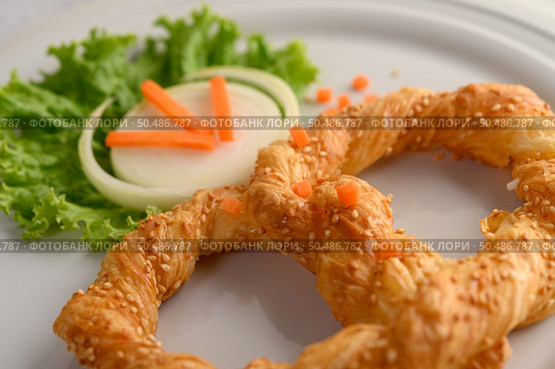Freshly baked soft pretzel with generous sprinkling of coarse salt and sesame on white dish, decorate with lettuce and carrot beautifully, copy space. Стоковое фото, агентство Ingram Publishing / Фотобанк Лори