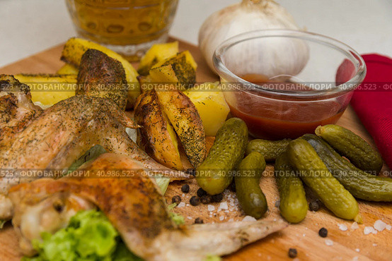 Fried chicken wings served on a wooden Board with Idaho potatoes, pickled gherkins and fresh lettuce leaves. A mug of beer is next to it. жареные куриные крылышки подаются на деревянной доске с картофелем Айдахо, маринованными корнишонами и свежими листьями салата. Рядом с ним стоит кружка пива. Стоковое фото, фотограф Дмитрий Березнев / Фотобанк Лори