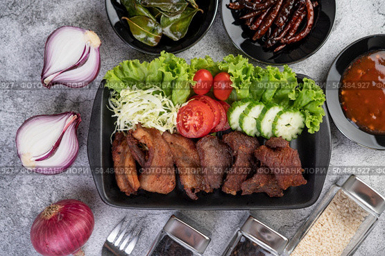 Fried pork topped with sesame, complete with tomatoes, cucumbers, cabbage, and lettuce placed in a black dish. Стоковое фото, агентство Ingram Publishing / Фотобанк Лори