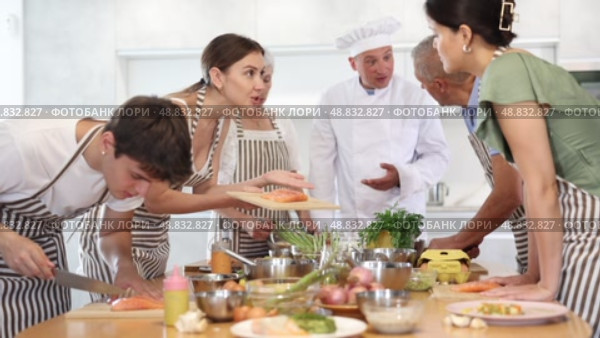 Friendly smiling young woman talking to culinary enthusiasts during group cooking masterclass from professional chef. Стоковое видео, видеограф Яков Филимонов / Фотобанк Лори