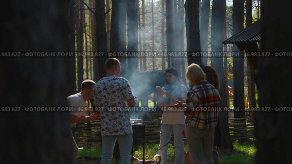 Friends are standing at barbecue and cooking meat in forest. Стоковое фото, фотограф David Kashakhi / Фотобанк Лори