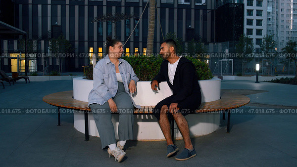 Friends man and woman sitting on wooden bench in a courtyard in new city region. Стоковое фото, фотограф David Kashakhi / Фотобанк Лори