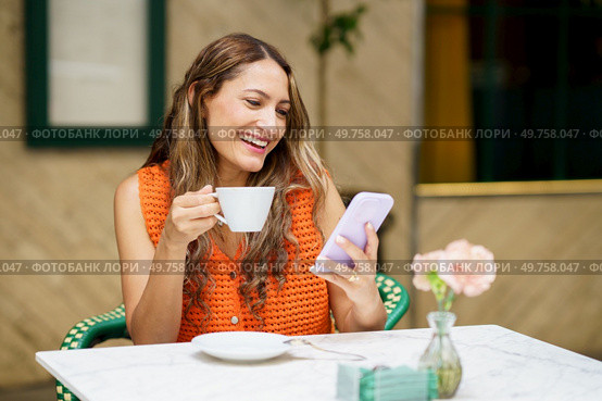 Frontal photo of a happy and relaxed latin woman smiling while using mobile phone in a cafeteria. Latin woman smiling while using mobile phone in a cafeteria. Стоковое фото, агентство Ingram Publishing / Фотобанк Лори