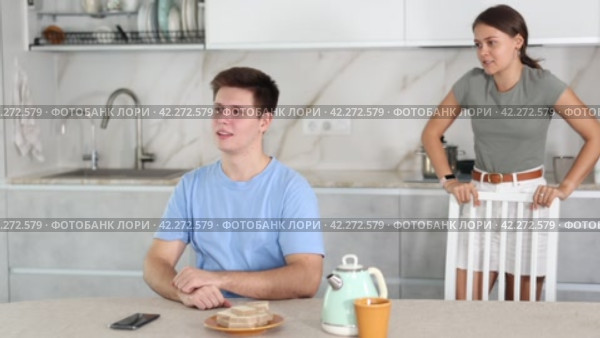 Frustrated offended guy sitting at kitchen table on background of swearing dissatisfied young wife. Family conflicts and communication problems concept. Стоковое видео, видеограф Яков Филимонов / Фотобанк Лори