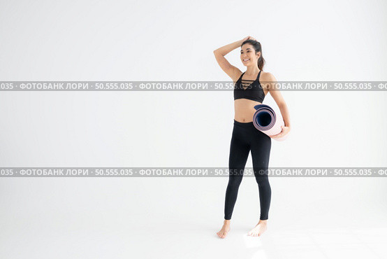 Full length portrait of a young woman holding yoga mat isolated on white background. Стоковое фото, агентство Ingram Publishing / Фотобанк Лори