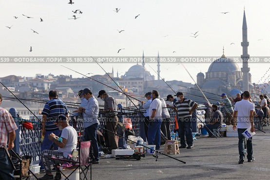 Galata Bridge with the New Valide Sultan Mosque in the background. Fishermen with fishing rods fishing from the bridge. City of Istanbul, Turkey. (2020 год). Редакционное фото, фотограф Bala-Kate / Фотобанк Лори