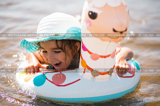 Girl in a hat it stands on the shore with inflatable circle in the shape of a lama. Inflatable alpaca for a child. Sea with a sandy bottom. Beach holidays, swimming, tanning, sunscreens. Стоковое фото, фотограф Ольга Симонова / Фотобанк Лори