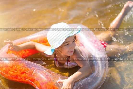 Girl in a hat swimming in the river with a transparent inflatable circle in the shape of a heart with orange feathers inside.The sea with a sandy bottom. Beach holidays, swimming, tanning, sunscreens. Стоковое фото, фотограф Ольга Симонова / Фотобанк Лори