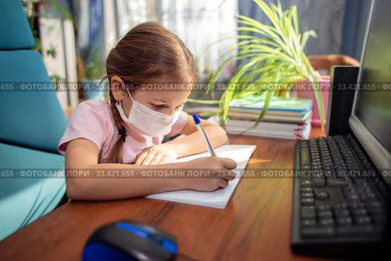 Girl schoolgirl in a medical mask does homework in front of a computer. Quarantine and distance learning. Стоковое фото, фотограф Екатерина Кузнецова / Фотобанк Лори