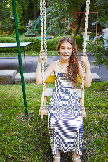 Girl sits on swings on a sunny day in green park. Стоковое фото, фотограф Losevsky Pavel / Фотобанк Лори
