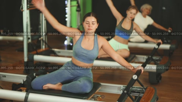 Girl sitting on foldable bed reformer performs exercises, strengthening body and muscles. Стоковое видео, видеограф Яков Филимонов / Фотобанк Лори