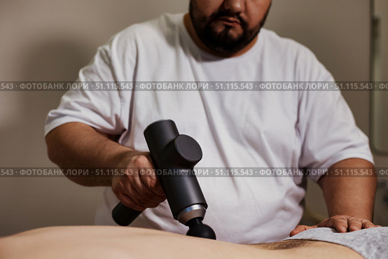 Giving Muscle Tension Relief With a Percussion Massager. Стоковое фото, фотограф Aleksandr Golubev / Фотобанк Лори