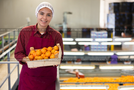 Glad positive female employee in colored uniforms hold a box of fresh ripe tangerines in their hands on citrus sorting line at warehouse. Стоковое фото, фотограф Яков Филимонов / Фотобанк Лори