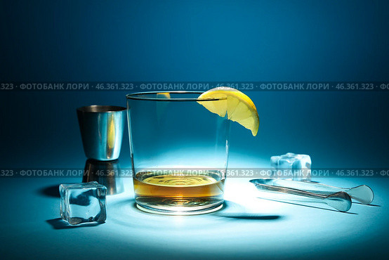 Glass of rum with ice cubes, lemon slice, tongs and jigger on dark blue background. Стоковое фото, фотограф Pixel_shot / Фотобанк Лори