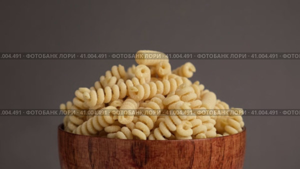 Gluten Free Cornmeal Pasta in wooden Bowl. Spiral Raw Macaroni from Blend of Corn and Rice flour rotating on Turntable. Close Up, Front View. Uncooked Rotini Pasta is Spinning. Food Background. Ad. Стоковое видео, видеограф Марина Демидюк / Фотобанк Лори