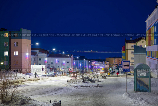 Город Анадырь, Чукотка, Россия. Вечерний городской пейзаж. Вид на улицу Отке и красочные разноцветные здания в благоустроенном северном городе. Вдали по заснеженному тротуару идут пешеходы. Путешествие на Дальний Восток России. Арктический регион. Редакционное фото, фотограф Андрей Степанов / Фотобанк Лори