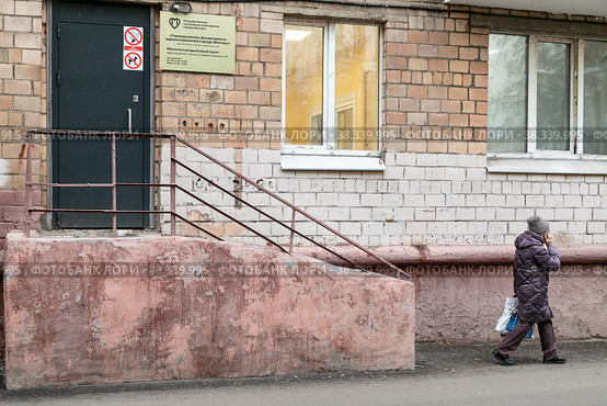 Город Москва, СВАО, улица Академика Комарова, 9а. Женщина вышла из молочно-раздаточного пункта, идет вдоль дома и разговаривает по телефону (2022 год). Редакционное фото, фотограф Наталья Николаева / Фотобанк Лори