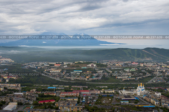 Город Петропавловск-Камчатский, Камчатский край, Дальний Восток России. Красивый городской пейзаж. Вид сверху на собор, здания и улицы. Вулканы вдалеке. Пасмурная погода. Низкая облачность. Стоковое фото, фотограф Андрей Степанов / Фотобанк Лори