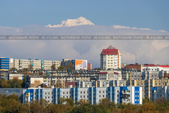 Город Петропавловск-Камчатский, Камчатский край, Россия. Вид на жилые дома на фоне гор. Вдалеке над облаками возвышается заснеженная вершина вулкана. Красивый городской пейзаж. Путешествие на Камчатку. Дальний Восток России. Редакционное фото, фотограф Андрей Степанов / Фотобанк Лори