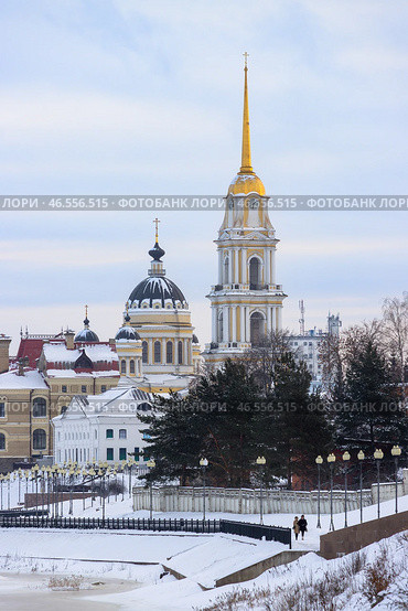 Город Рыбинск, Ярославская область, Россия. Зимний вид на Спасо-Преображенский кафедральный собор и Волжскую набережную. По заснеженной набережной реки Волги гуляют люди. Вдали высокая колокольня с позолоченным шпилем и часами. Архитектурные туристические достопримечательности Рыбинска. Путешествия и туризм по регионам России. Редакционное фото, фотограф Андрей Степанов / Фотобанк Лори