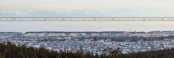 Город Северобайкальск, Республика Бурятия, Сибирь, Россия. Вид сверху на город Северобайкальск, расположенный на берегу озера Байкал. Зимний городской пейзаж. Вдали заснеженные горы. Озеро покрыто льдом. Широкая панорама. Стоковое фото, фотограф Андрей Степанов / Фотобанк Лори