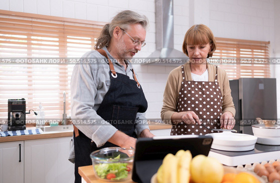 Grandparents are having a good time in the kitchen preparing dinner for their daughter and grandchildren. Previewing cooking examples online. Стоковое фото, агентство Ingram Publishing / Фотобанк Лори