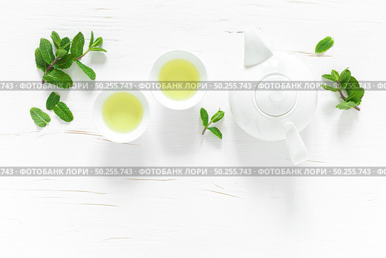 Green mint tea with fresh leaves in cups and teapot overhead on white wooden table, healthy warming drink, antioxidant beverage, top view. Стоковое фото, агентство Ingram Publishing / Фотобанк Лори
