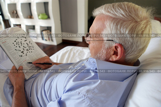 Grey-haired man completing crossword puzzle. Стоковое фото, агентство Ingram Publishing / Фотобанк Лори