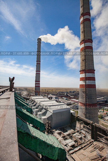 Grey raw coal bunkers on front. Smoke stacks with white smoke both sides. Dry steppe, blue sky on background. Ekibastuz, Pavlodar reg., Kazakhstan. GRES-1 thermal power station. Стоковое фото, фотограф Alexey Rezvykh / Фотобанк Лори