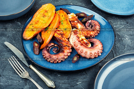 Grilled or roasted octopus tentacles garnished with baked sweet potato wedges. Food photography.. A dish with roasted octopus tentacles. Стоковое фото, агентство Ingram Publishing / Фотобанк Лори
