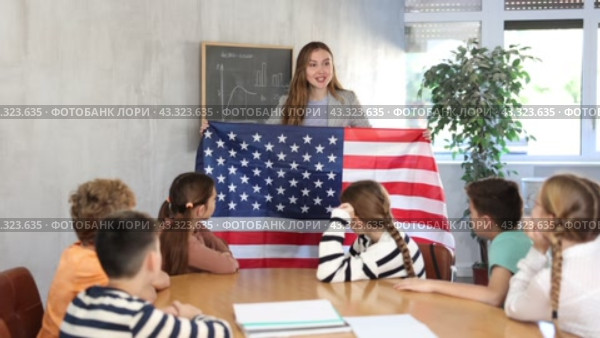 Group of curious preteen learners and young female teacher with flag of USA in classroom of academy. Стоковое видео, видеограф Яков Филимонов / Фотобанк Лори