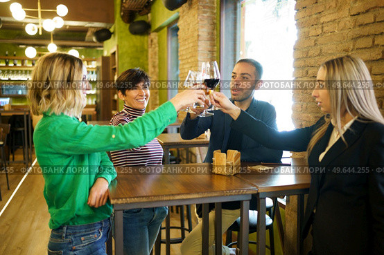 Group of multiracial people smiling and clinking glasses of alcohol beverages over table while proposing toast during meeting in bar. Diverse friends clinking glasses over table in beautiful pub. Стоковое фото, агентство Ingram Publishing / Фотобанк Лори
