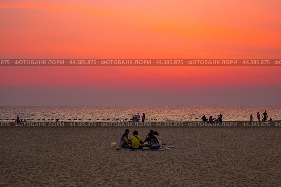 Group of people, family sitting on sand, having a picnic at sunset by the sea. Thailand, Pattaya (2024 год). Редакционное фото, фотограф Коханова Наталья / Фотобанк Лори