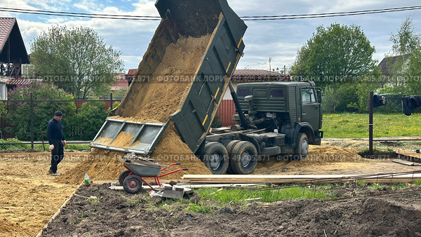 Грузовой самосвал выгружает песок на строительной площадке. Редакционное фото, фотограф Антон Моргунов / Фотобанк Лори