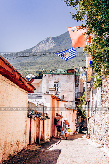 Gurzuf, Crimea, 6 July 2020, People walk along narrow urban street in small town. Редакционное фото, фотограф Spirit River / Фотобанк Лори