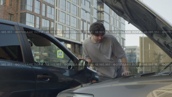 Guy studies scene of the accident, where the car collided with another, to assess the potential damage and the cost of repairs. Стоковое видео, видеограф Strunov David / Фотобанк Лори