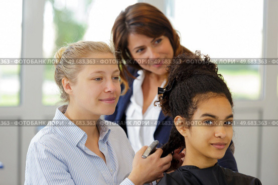 hairdressing apprentice learning to iron clients hair. Стоковое фото, агентство Ingram Publishing / Фотобанк Лори