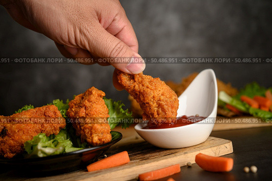 Hand holding crispy fried chicken dipped in tomato sauce. Selective focus. Стоковое фото, агентство Ingram Publishing / Фотобанк Лори