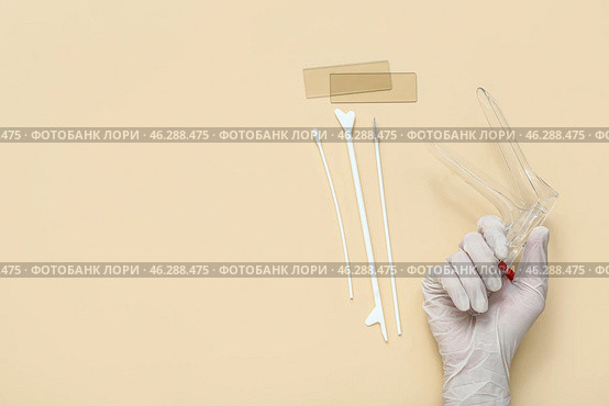 Hand in medical glove, with gynecological speculum and pap smear test tools on beige background. Стоковое фото, фотограф Pixel_shot / Фотобанк Лори