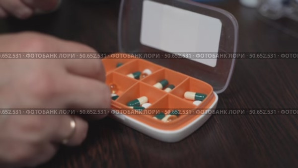 Hand placing light-yellow vitamin D capsules into a weekly pill organizer for medication management. Стоковое видео, видеограф Татьяна Степанищева / Фотобанк Лори
